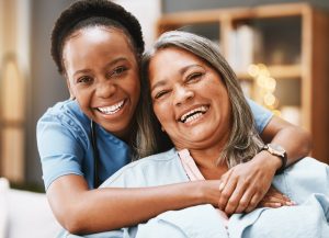 A caregiver providing 24-hour care to help a senior age at home hugs an older loved one as they laugh.