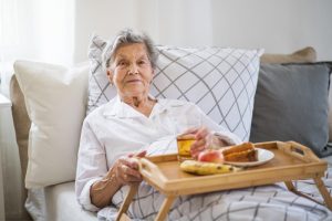 An older woman experiencing end-of-life nutrition challenges sits in bed with a tray of uneaten food on her lap.