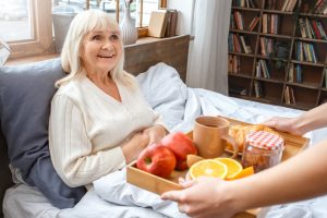 A woman receives a healthy breakfast in bed from her caregiver to help ease some of the common challenges seniors face after surgery.