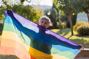 A woman receiving LGBTQ+ senior care holds up a pride flag.