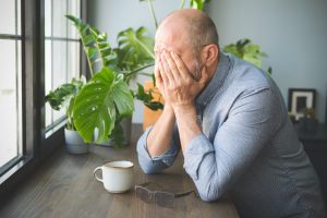 A man struggling with senior post-traumatic stress disorder holds his face in his hands.