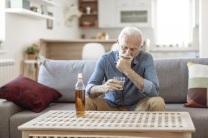 An older man holds a glass of whiskey, pondering older adults and substance abuse and wondering if he might be at risk.