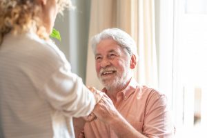 A man coming home after a stroke smiles as his caregiver helps him to stand.