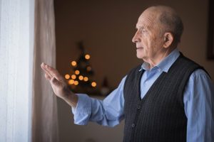 An older man shows signs of depression in seniors as he looks pensively out his window during the holiday season.