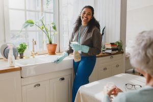 A caregiver smiles as she cleans the kitchen for an older woman who understands the truths behind common misconceptions about home care.