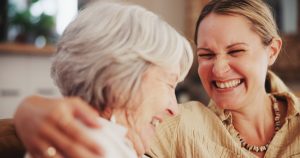 A caregiver laughs with an older woman, knowing that companionship is key to mental and emotional health in seniors.