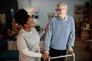 A caregiver helps with preventing falls after surgery as she helps an older man walk safely with his walker.