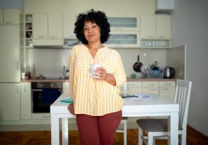 A woman smiles confidently with a cup of coffee in her hand after learning about setting boundaries as a caregiver.