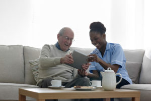 Happy senior man and nurse using digital tablet at home