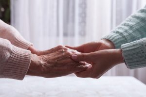 A pair of older hands holds a pair of younger hands, symbolizing supporting mental health in aging parents.