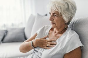 Senior woman sitting down with a hand on her chest