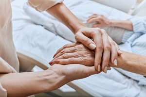 A woman’s hands hold an elderly hand, indicating Alzheimer’s end-of-life care.