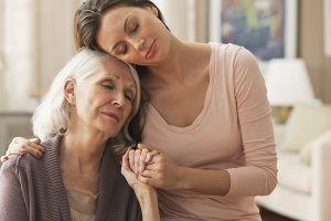 An older woman with a chronic health condition receives a hug from her daughter.