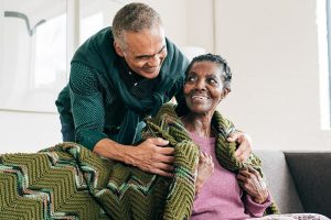 A man wraps a blanket around an older woman, learning from Alzheimer’s caregiving mistakes how to provide better care.