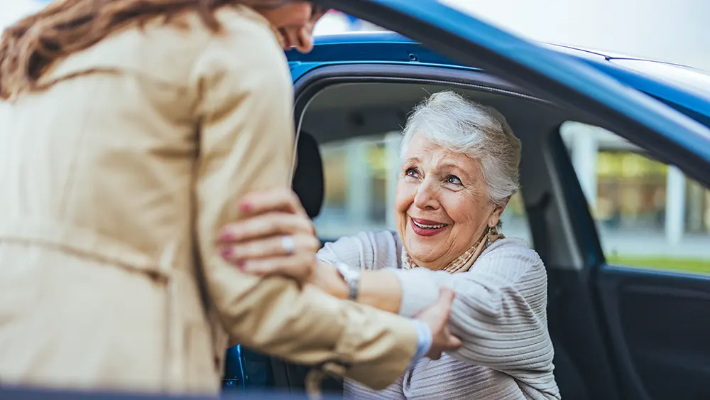 Companion Care in the Greater Burlington Area A caregiver providing senior transportation services in Burlington helps an older woman get out of her car.
