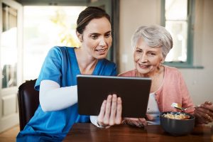 A nurse shows an older woman some important information on a tablet after her heart surgery.