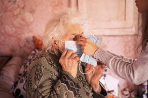 caregiver helping senior woman with mask