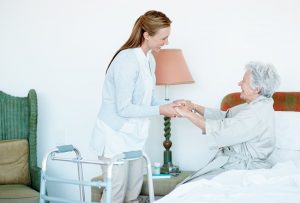 A caregiver practices the right protocol for lifting a senior as she helps an older woman out of bed.