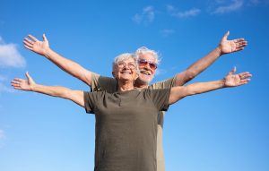 Two older adults express freedom from living with chronic pain by spreading their arms wide against the background of a blue sky.