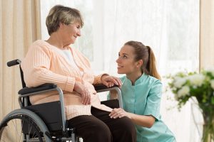 A caregiver talks to an older woman before using the best practices for transferring a senior from her wheelchair.