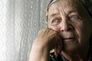 Senior woman looking through the window with a sad expression