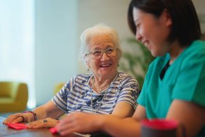 An occupational therapist guides an older woman through an activity at home.