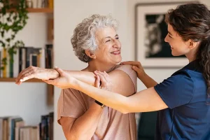 A physical therapist helps an older woman with a stretching exercise.