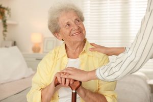 Empowering You to Live Well An older woman receiving respite care services leans on her cane and smiles as her caregiver places a hand on her shoulder.
